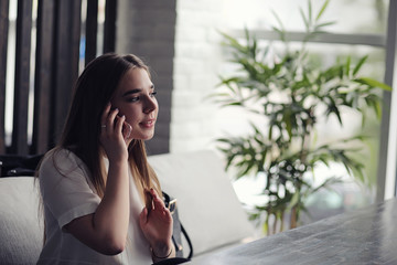 Young girl in a cafe. The girl is sitting on the couch and talking on the phone.