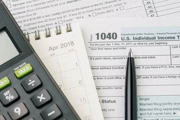 Tax time in April concept, pen on 1040 US individual income tax filling form with calendar and calculator