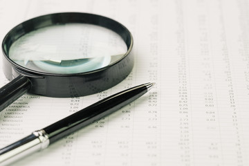 Business perfomance review, searching or chasing for investment return concept, magnifying glass and pen on performance, price numbers report print paper on table