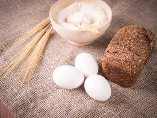 Flour, ears of wheat, black bread, eggs on a background of cloth. Cooking bread