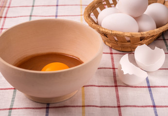 Basket with eggs, wooden bowl with yolk on the table. Cooking food