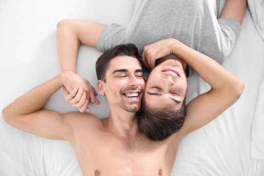 Young gay couple lying on bed, top view