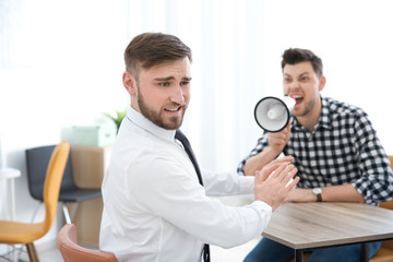 Angry boss with megaphone screaming at employee in office