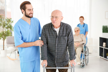 Senior man with walking frame and young caregiver at home