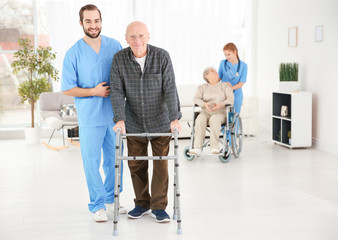 Senior man with walking frame and young caregiver at home