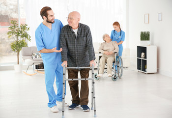 Senior man with walking frame and young caregiver at home