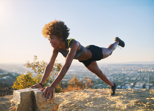 athletic young african american woman doing stretches and pushups at runyon canyon with view of los angeles in background