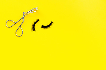 Curled and thick eyelashes. False eyelashes and eyelash curler on yellow background top view copy space