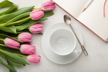 Empty white cup of coffee and a bunch of pink tulips on the pastel white table background, top view, flat lay