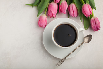 Black coffee in white Cup with pink tulips on light stone background. Top view with copy space