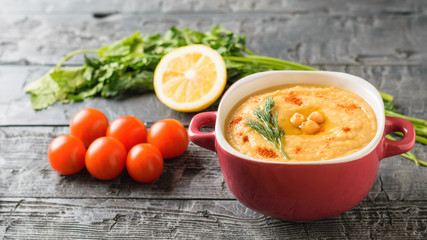 Freshly made hummus in a purple bowl and six cherry tomatoes on a dark wooden table.