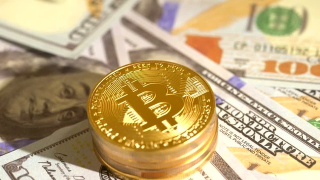 Bitcoin coins rotating on a pile of 100 dollar bills