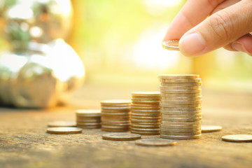 Saving money concept with Hand putting money coin stack growing business on abstract sunset background	
