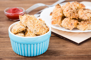 Homemade nuggets from chicken in a bowl and on a plate  on a wooden table