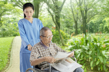 Elderly man reading newspaper with his nurse