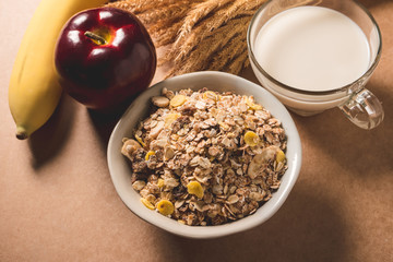 Oatmeal flakes in a bowl, milk, apple and banana on wooden table. Healthy breakfast concept.