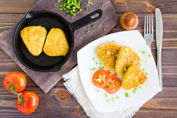 Crispy hash browns on a plate and in a pan and tomatoes on a wooden table. Top view