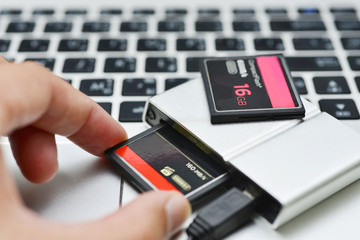Hand holding compact flash memory card in card reader on keyboard notebook background