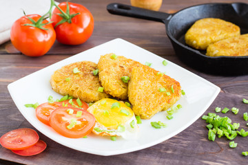 Crispy hash browns, chiken egg and tomatoes on a plate on a wooden table