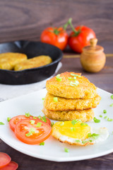 Pile of crispy hash browns, chiken egg and tomatoes on a plate on a wooden table