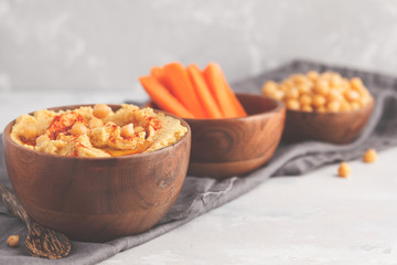 Hummus, fresh carrot sticks and boiled chickpeas in wooden bowls. Vegan food concept, light background, copy space.