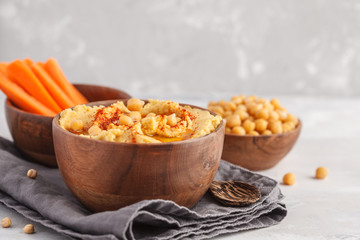 Hummus, fresh carrot sticks and boiled chickpeas in wooden bowls. Vegan food concept, light background, copy space.