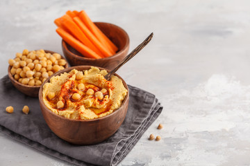 Hummus, fresh carrot sticks and boiled chickpeas in wooden bowls. Vegan food concept, light background, copy space.