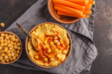 Hummus, fresh carrot sticks and boiled chickpeas in wooden bowls. Vegan food concept, dark background, copy space, top view