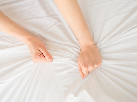 Female hands clutching white bedsheets. Sensual concept