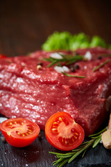 Composition of raw beefsteak on slate board with vegetables and seasoning, selective focus, close-up, vertical