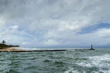 ocean coast, waves, sky, clouds, flock of pelicans flying in height, old lighthouse, breakwater