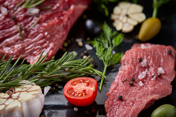 Flat lay of raw beefsteak with vegetables, herbs and spicies on metal tray, close-up, selective focus