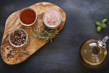 Close-up photo of colored dried spices in bowls on wooden board on black concreted table background with olive oil in jar