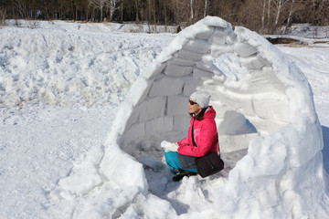 Happy woman in a red jacket sitting in unfinished an igloo   on a snowy glade, Siberia, Russia