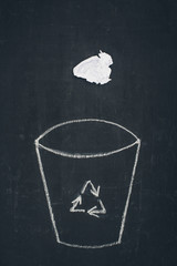 crumpled paper falling into drawn trash bin with recycle sign on chalkboard