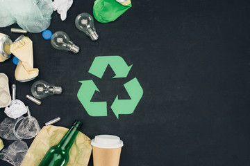 top view of various types of trash with recycle sign on black