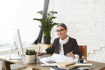 Portrait of successful attractive mature female engineer in her fifties wearing rectangular glasses...