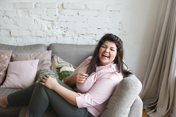 Happy attractive young obese overweight female model laughing at joke or funny story, relaxing in...
