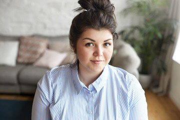 Close up shot of gorgeous overweight chubby young dark haired lady wearing striped blue shirt...