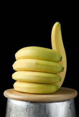 bananas lying on a wooden board in the shape of a hand with the thumb up, on a black background...