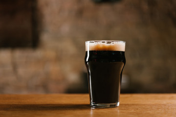 glass of fresh cold dark beer on wooden table in pub