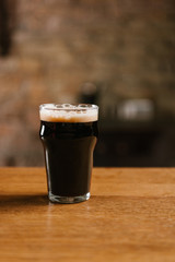 fresh cold dark beer with foam in glass on wooden table in pub