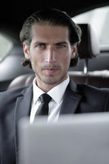 man sitting in the back-seat of a car, using his laptop