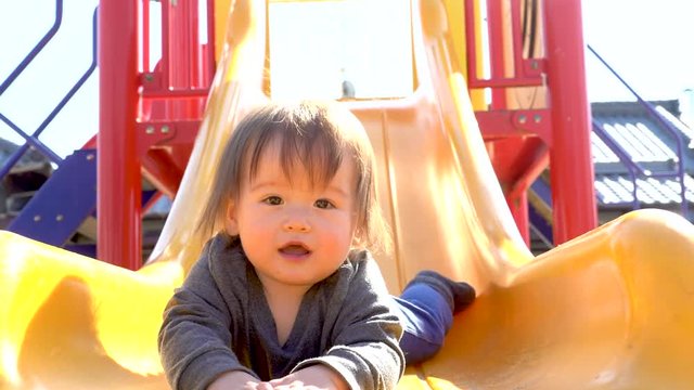 Happy toddler sliding down the slide at the playground