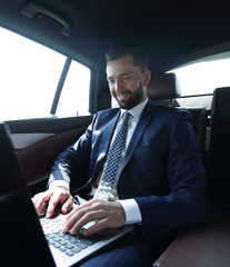 businessman sitting in the back-seat of a car, using his laptop