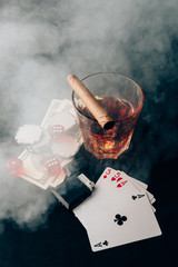 Glass with whiskey and cigar on table with cards and money
