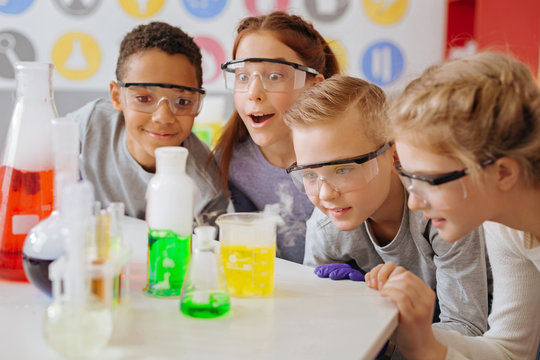 Fond of chemistry. The group of upbeat teenage students being gathered around the table in their school lab and observing the final stage of their chemical experiment with excitement
