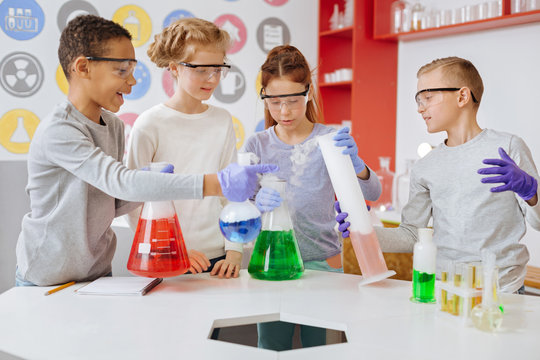 Involved in experiment. The group of cheerful teenage students observing reactions in all kinds of chemical glassware and discussing them during their chemistry class in the lab