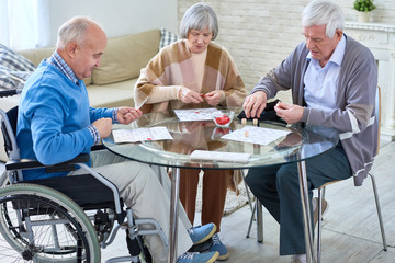 Group of senior people playing lotto game sitting at glass table in living room