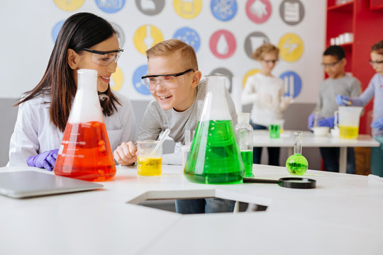 Upbeat ambience. Cheerful young chemistry teacher and her student sitting at the table in the lab and laughing while discussing a chemical experiment